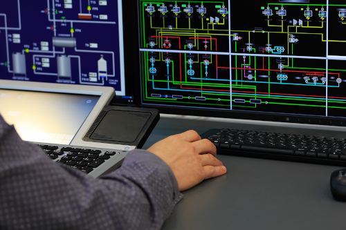 Hand clicking mouse with computer screen in front showing control systems diagram
